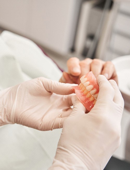 Gloved hands passing dentures to patient in dental chair