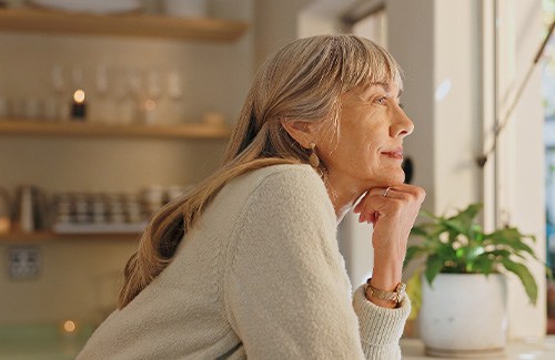 Senior woman smiling while looking out the window at home