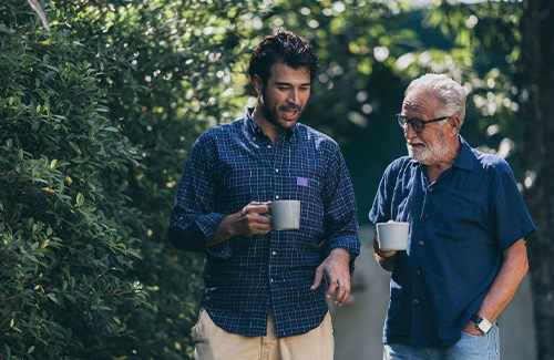 Younger and older man with mugs walking and talking outside