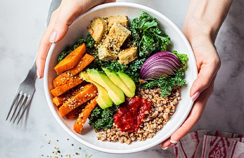 Hands holding white bowl of healthy salad ingredients