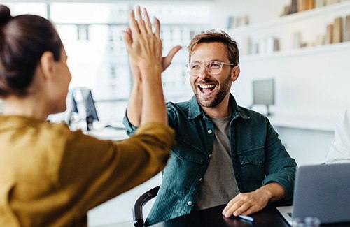 Man and woman at work desk with laptop high-fiving