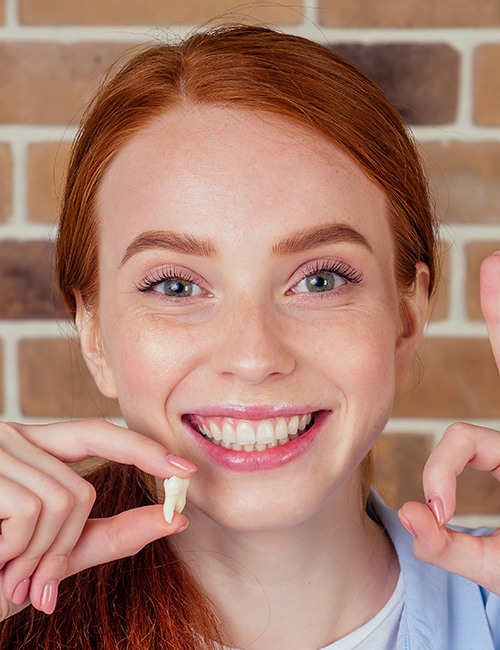 Woman with red hair holding extracted tooth making ok sign with other hand