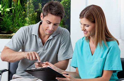 Man giving credit card to woman in scrubs holding clipboard