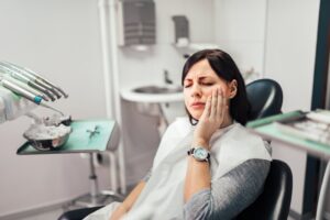 Woman in dentist's chair holding mouth in pain. 