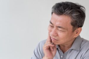 Man holding jaw in pain from denture sore.