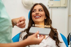 Woman smiling in dentist’s chair with staff holding veneers in foreground.